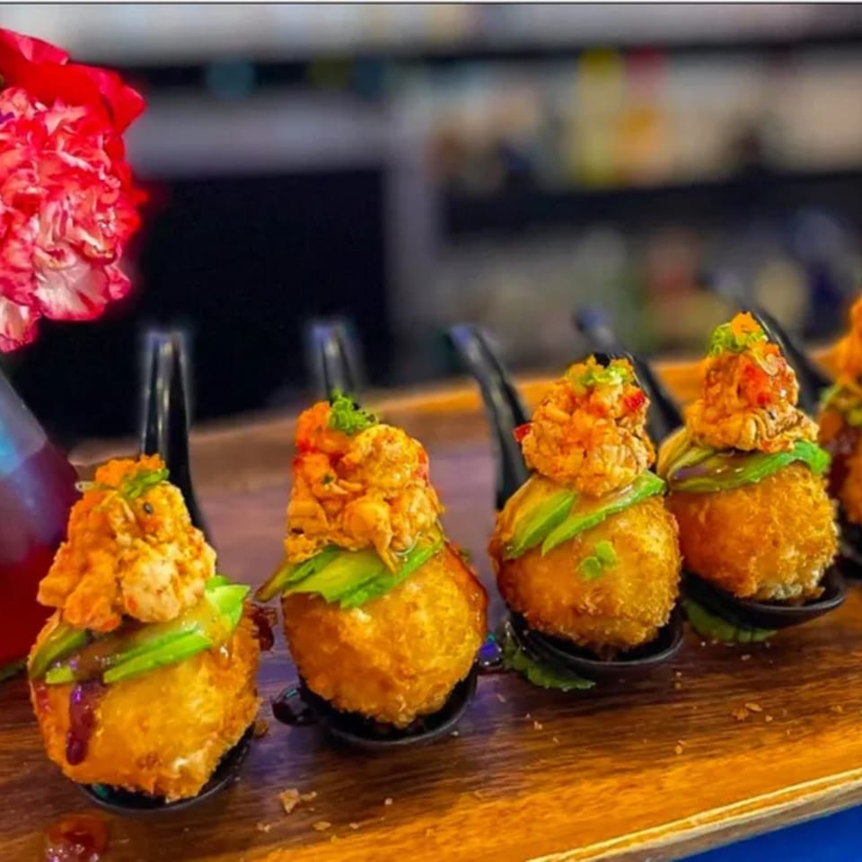 Golden fried sushi balls topped with spicy seafood, avocado, and sauce on a wooden board.