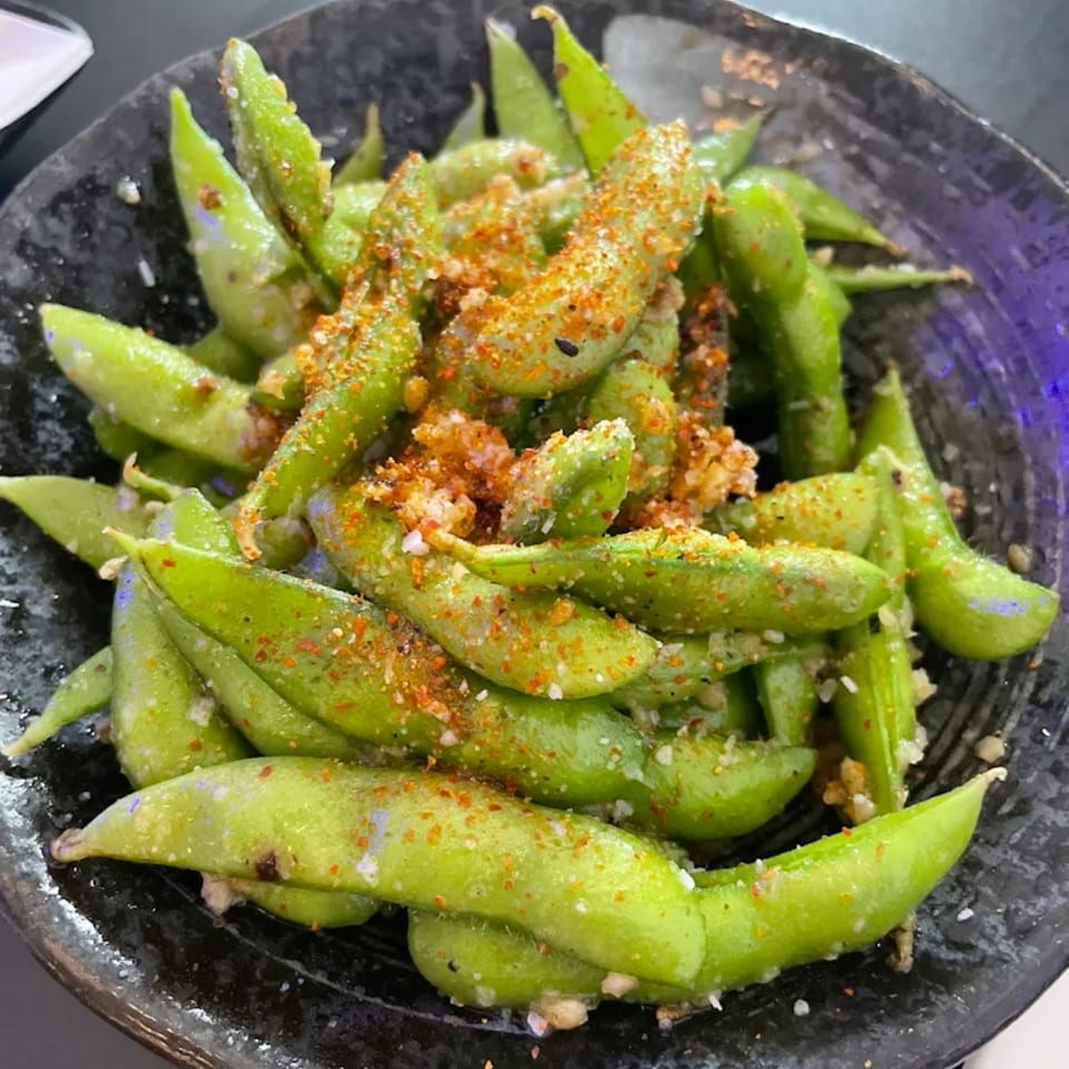 A close-up of edamame pods seasoned with spices and salt in a dark bowl at Bluefin Sushi Fusion.