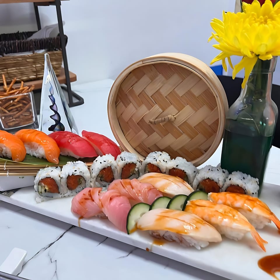 A platter of Blue fin Sushi Fusion's nigiri and maki rolls, with a bamboo steamer and yellow flowers.