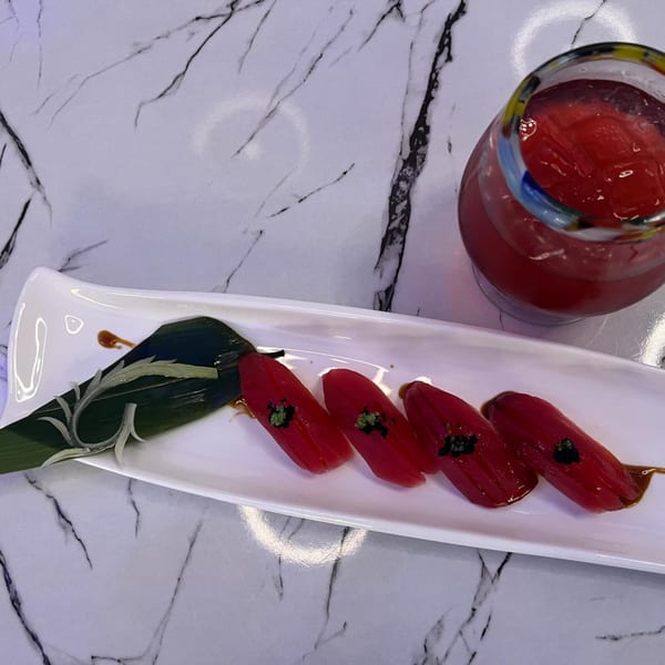 Four pieces of red tuna nigiri sushi with green garnish and a red drink on a marble table.