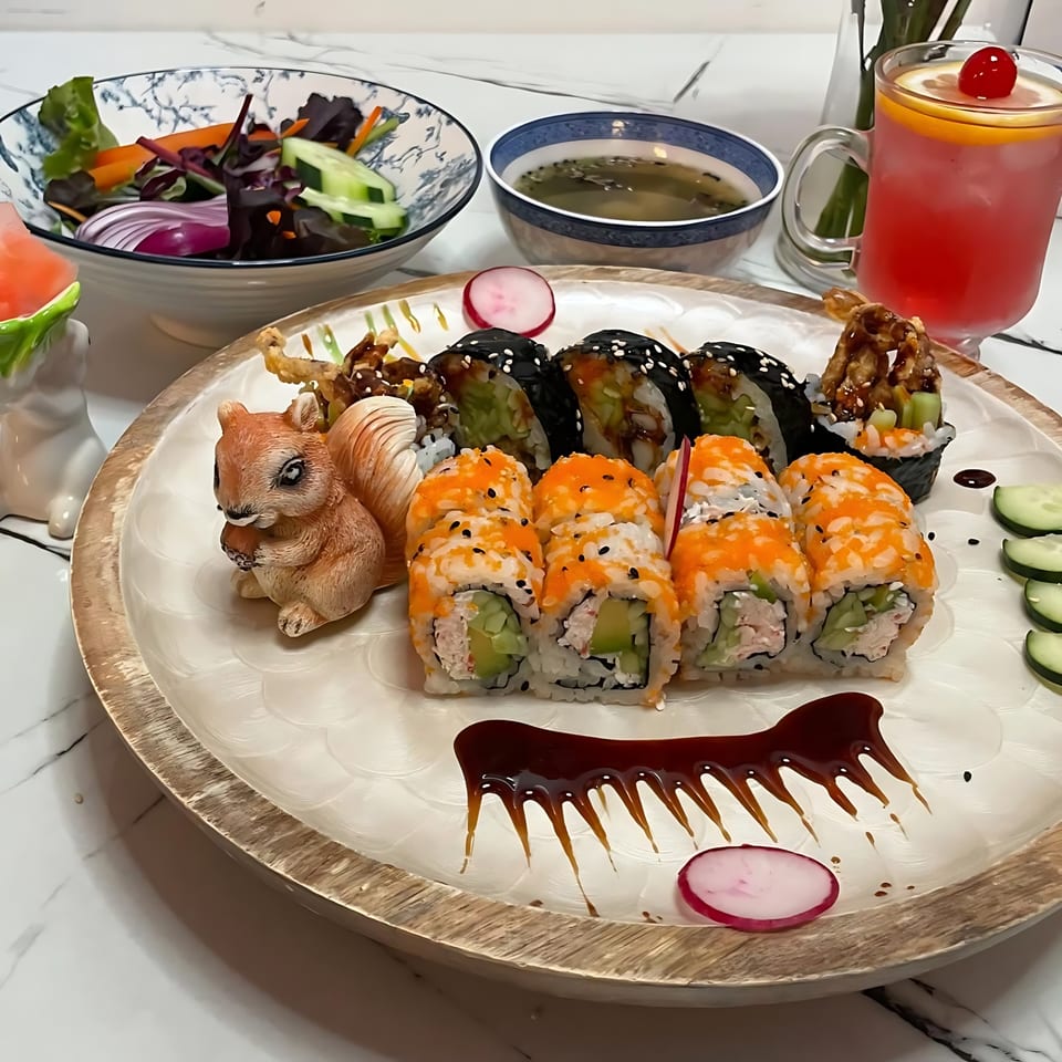 A sushi platter with various rolls, a side salad, soup, and a pink drink with a cherry.